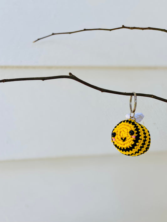 A yellow and black striped crochet bee keychain with a cute face and rosy cheeks