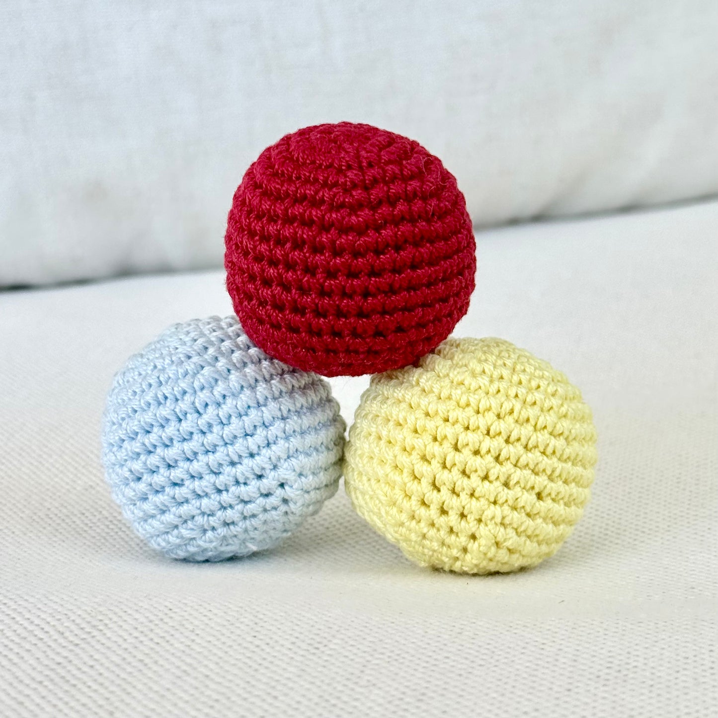 Three crocheted balls in red, blue, and yellow on a light fabric background