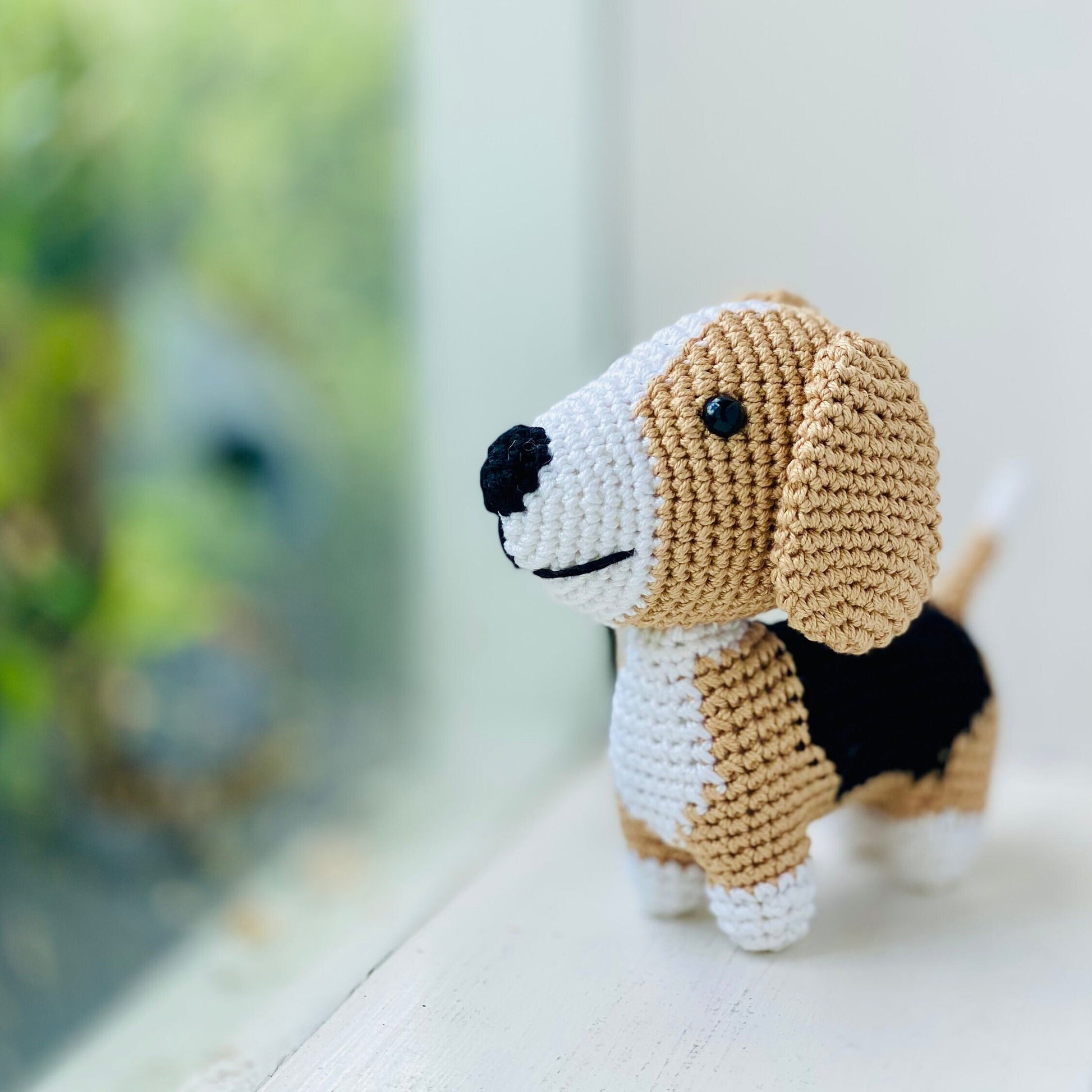 A crocheted beagle toy with floppy ears looking out the window.