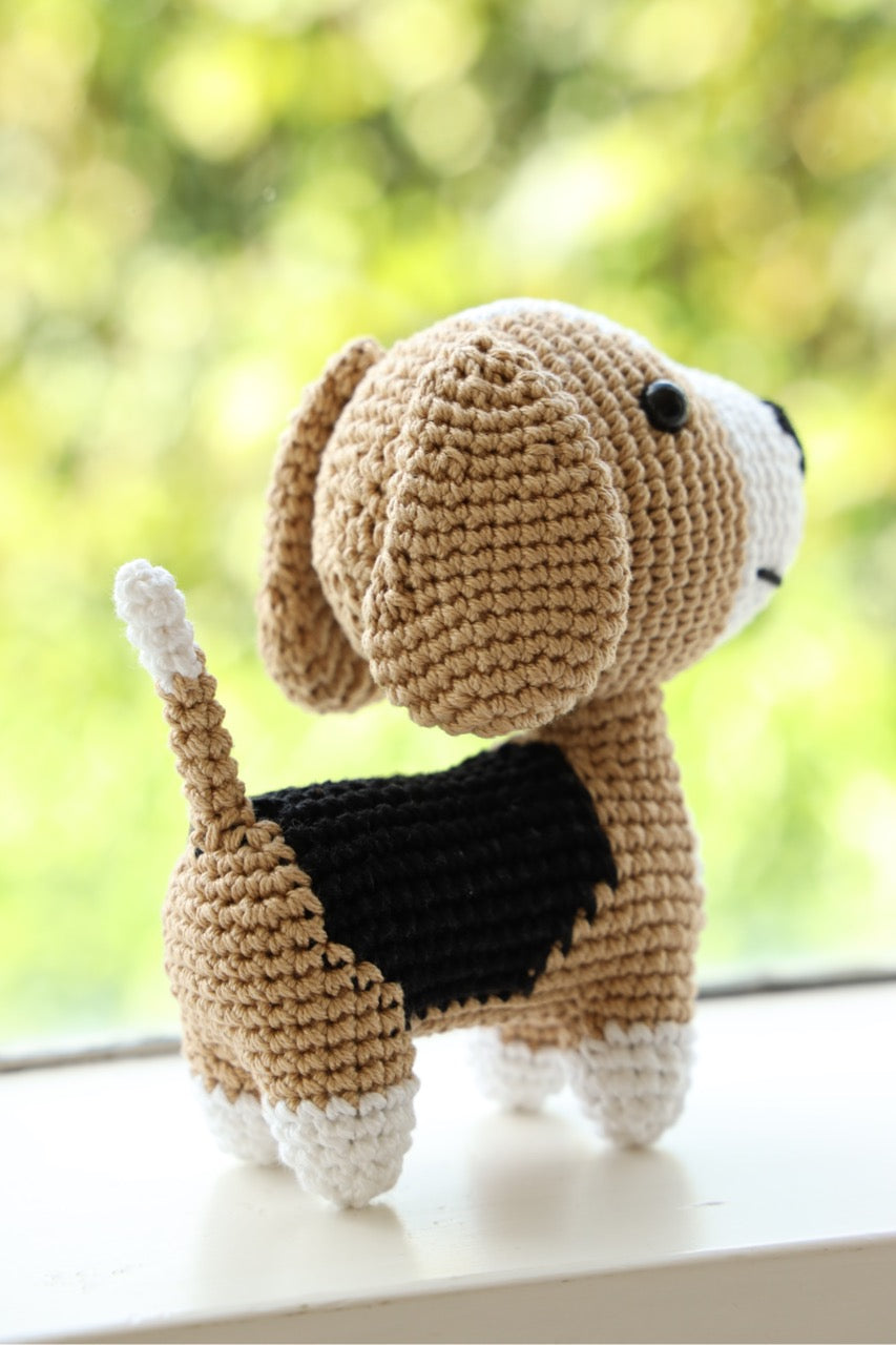 A crocheted beagle toy with floppy ears looking out the window