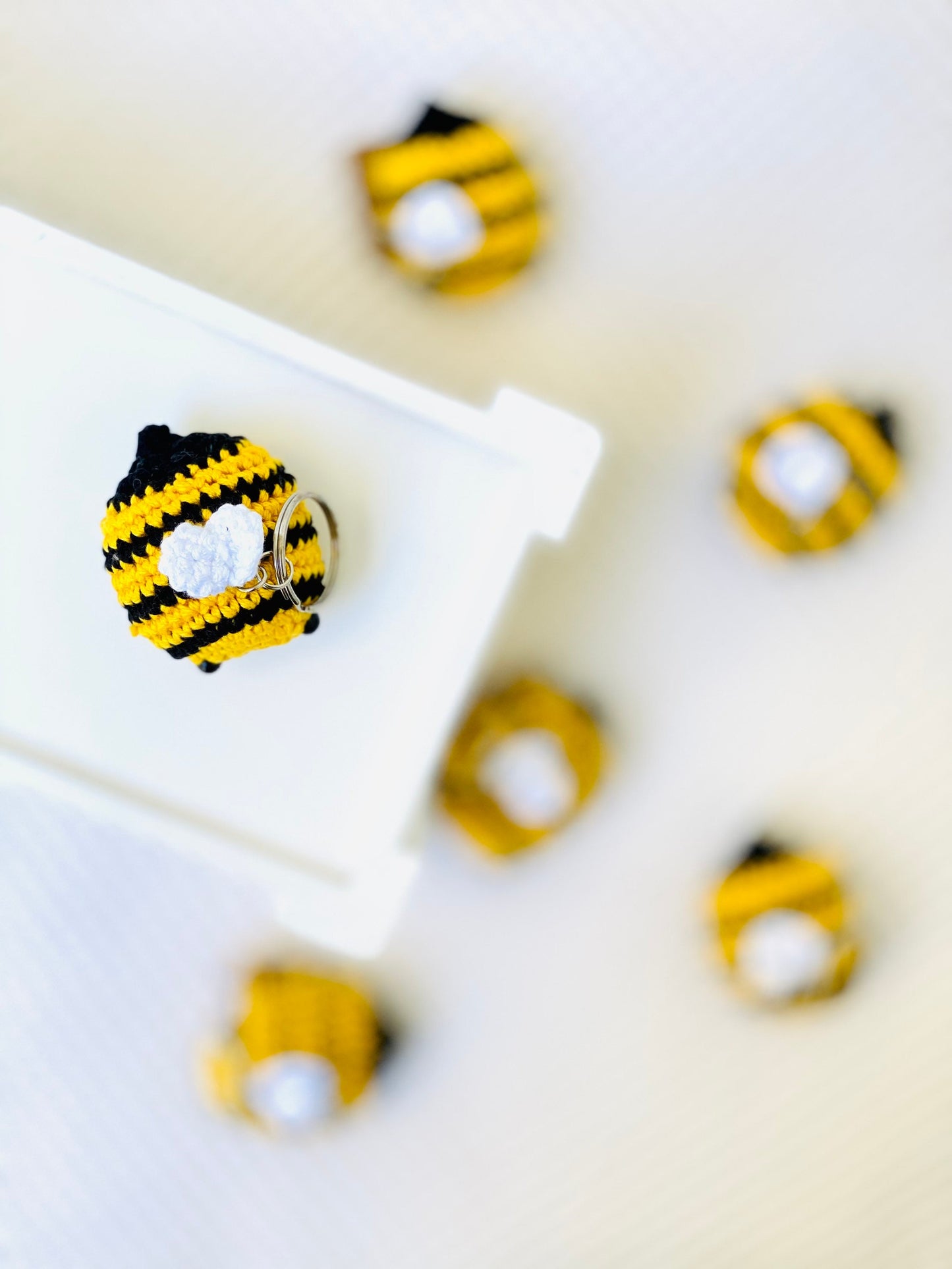 A collection of yellow and black striped crochet bee keychains with cute faces and rosy cheeks, displayed on a white surface.