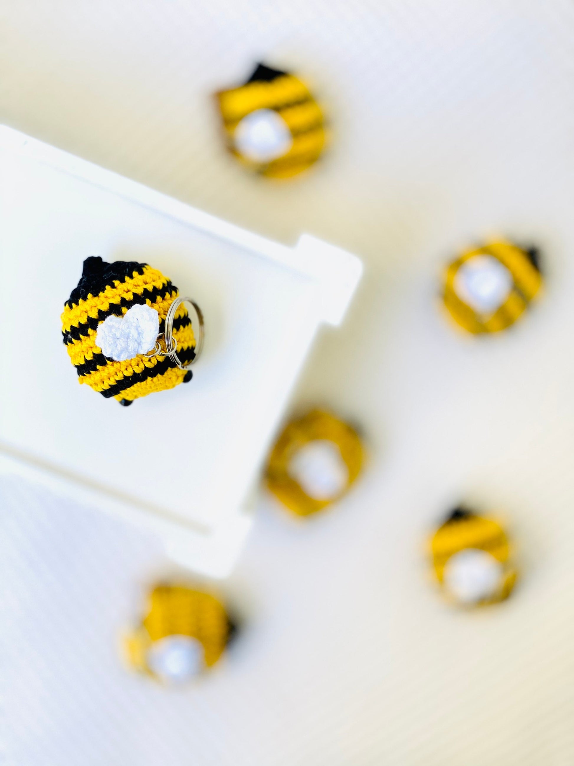 A collection of yellow and black striped crochet bee keychains with cute faces and rosy cheeks, displayed on a white surface.