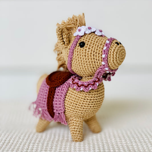 A small, brown embroidered horse with a purple saddle and floral detail, standing on a white background.