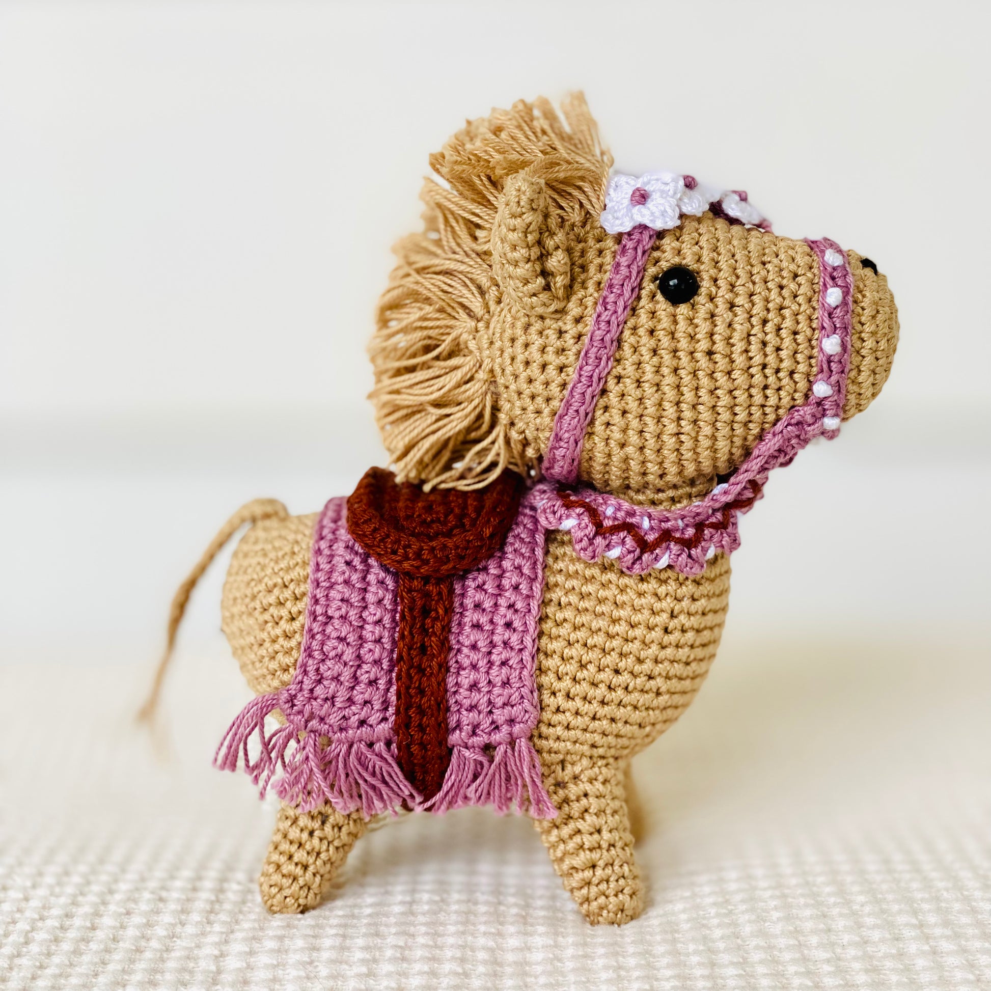 A small, brown embroidered horse with a purple saddle and floral detail, standing on a white background.