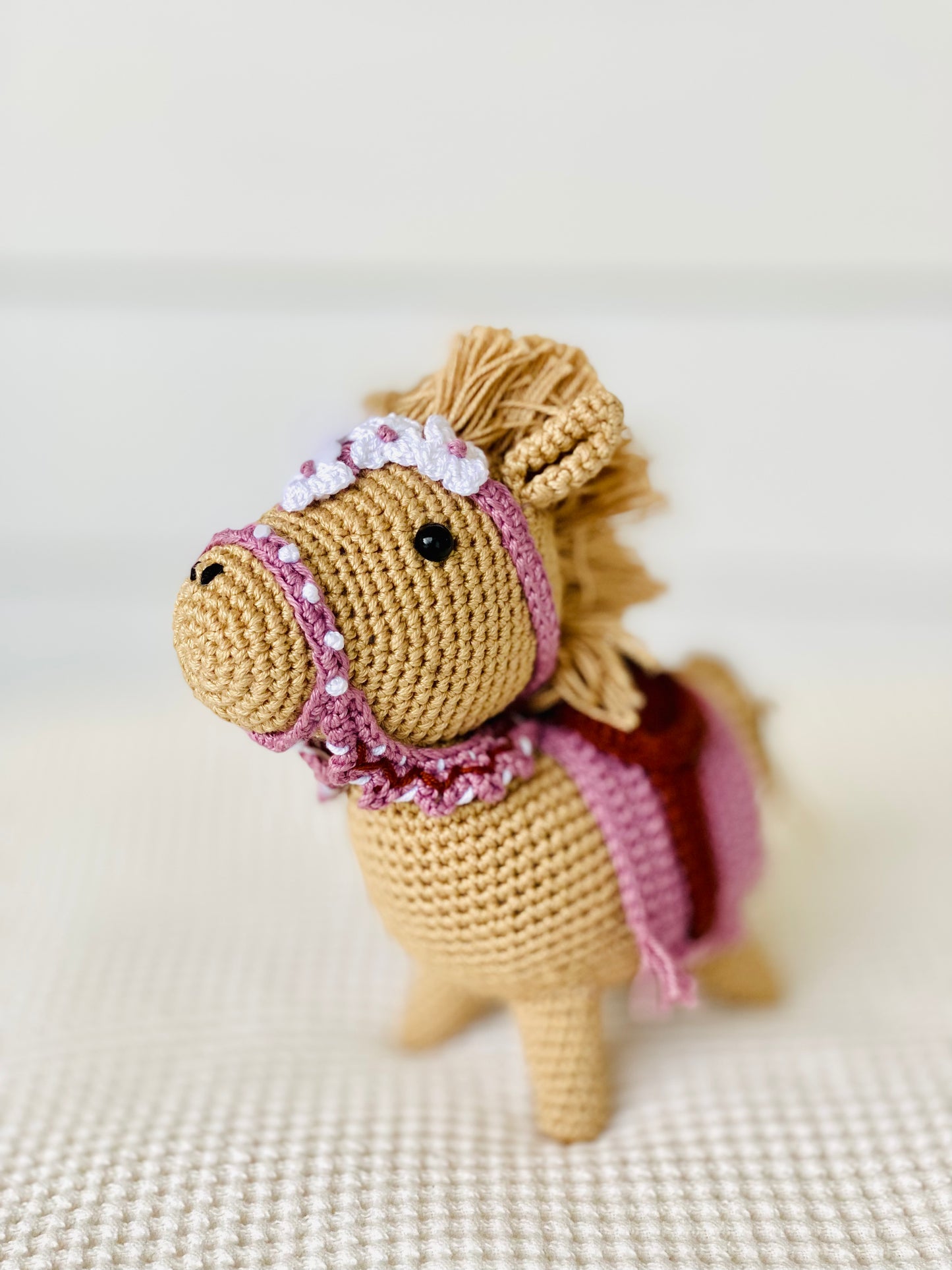 A small, brown embroidered horse with a purple saddle and floral detail, standing on a white background.