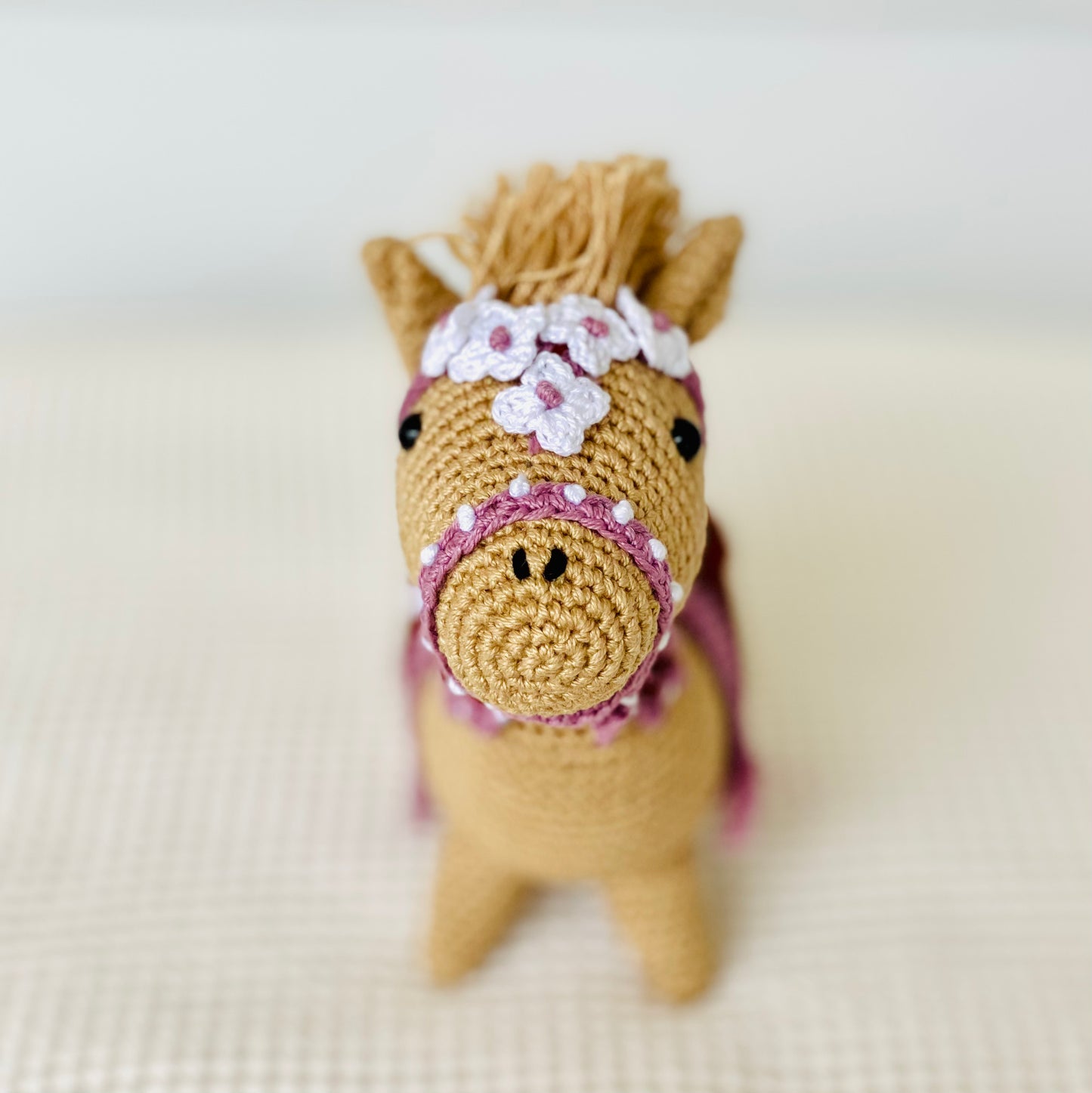 Front view of a small, brown embroidered horse with a purple saddle and floral detail, standing on a white background.